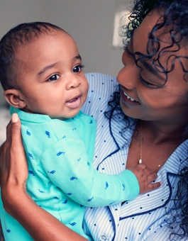 Loving African American Mother Wearing Pyjamas Cuddling Baby Daughter In Bedroom At Home